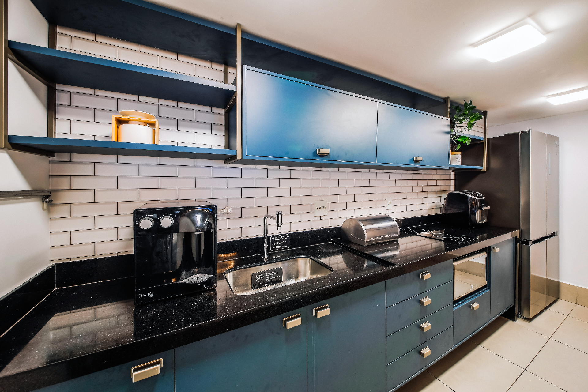Espaço gourmet completo com bancada em granito, cooktop, geladeira e armários em tons de azul