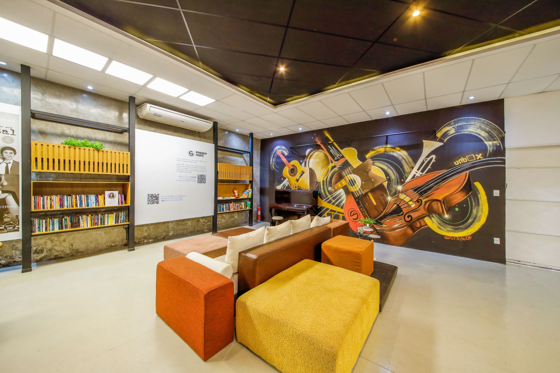 Lounge do Espaço Multi com sofás, piano e mural artístico